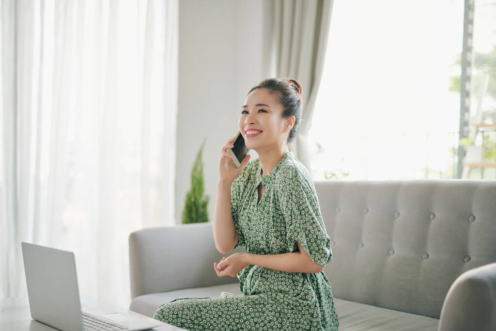 快乐的年轻女性自由撰稿人，一边用手机一边用笔记本电脑，一边在家里工作，复制空间. 